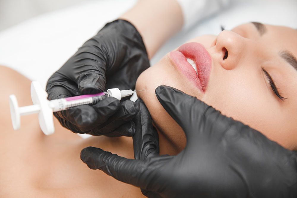 A gloved injector placing filler along a client's upper lip — dermal fillers in McAllen, TX
